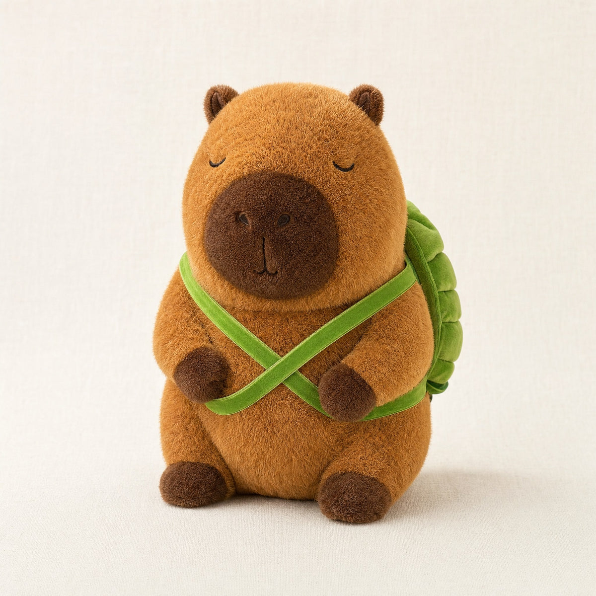 Peluche capybara marron avec sac à dos tortue vert, vue de face sur fond crème