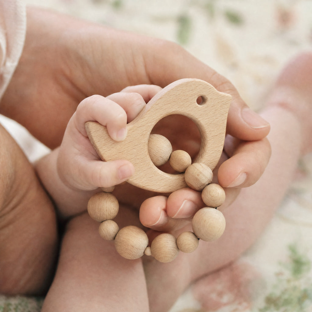 Bébé tenant l'anneau de dentition oiseau en bois avec la main d'un parent