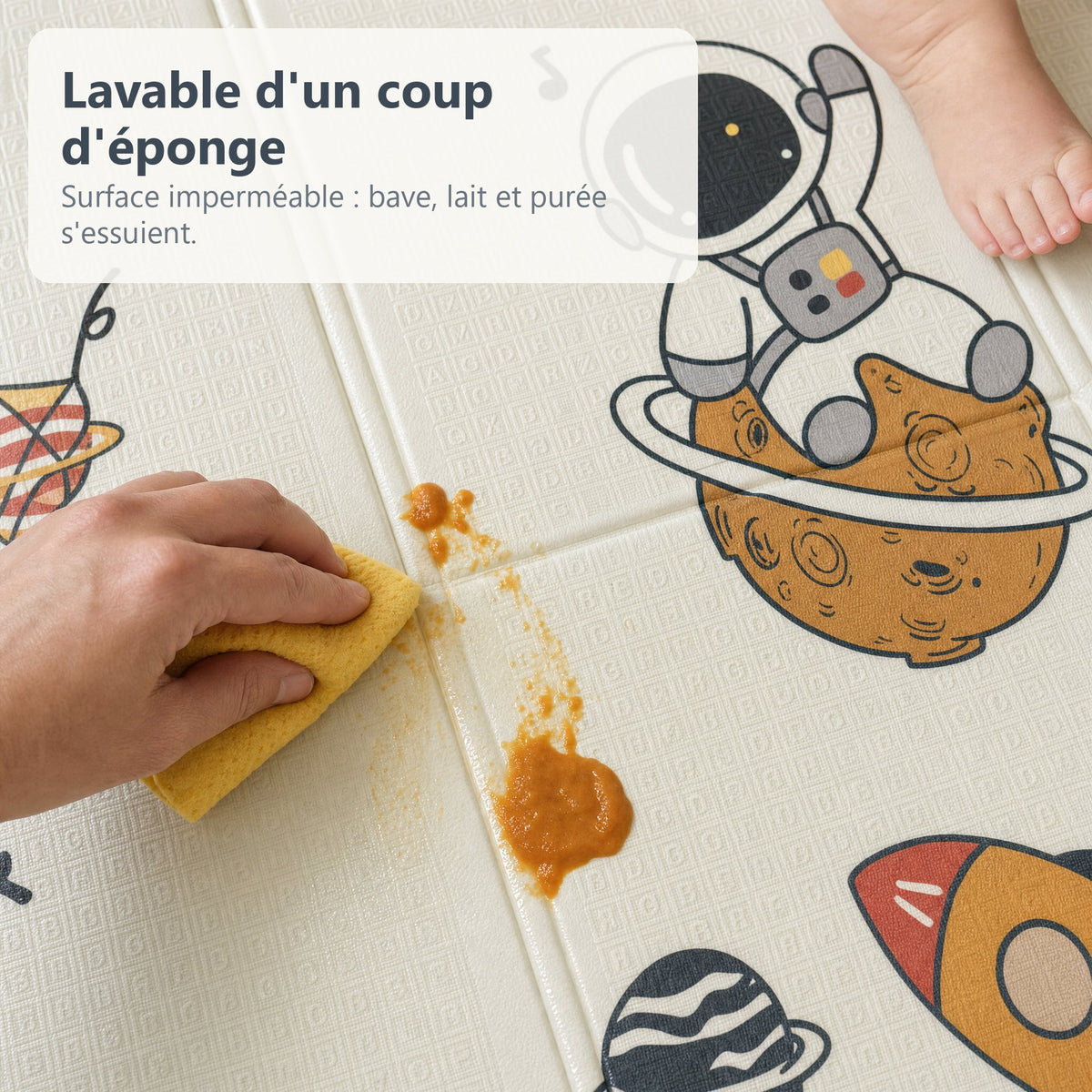 Une main essuie de la purée d'un coup d'éponge sur le tapis de jeu imperméable astronaute et planètes