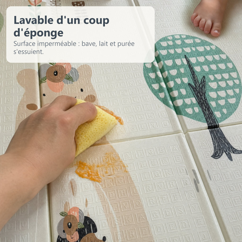 Une main essuie de la purée d'un coup d'éponge sur le tapis de jeu imperméable forêt et lion