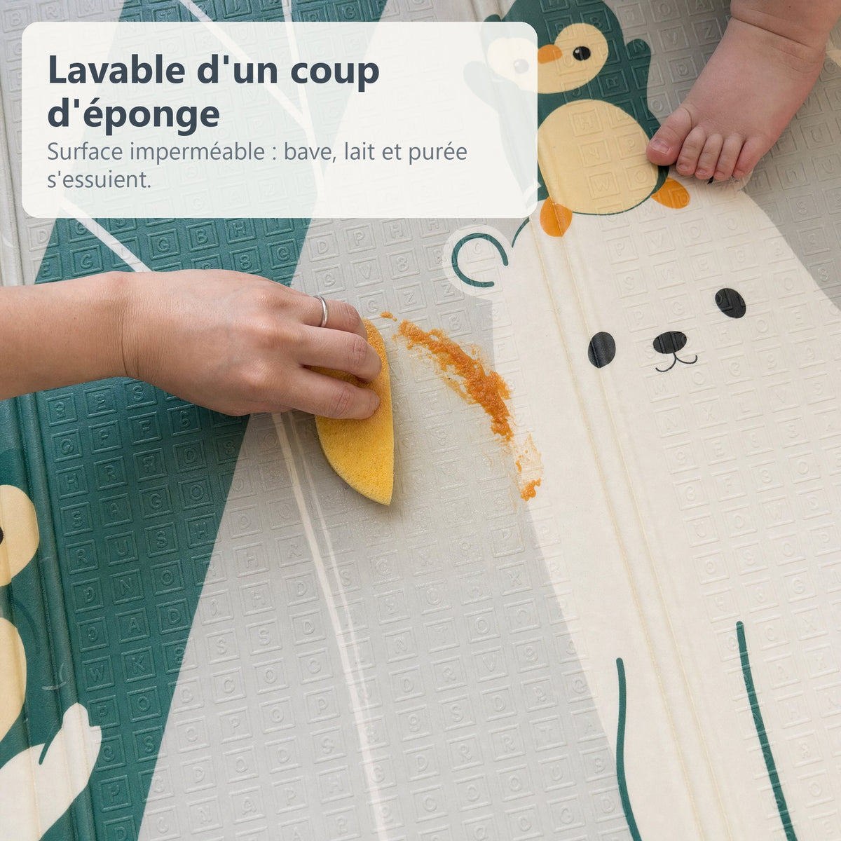 Une main essuie de la purée d'un coup d'éponge sur le tapis de jeu imperméable ours polaires et alphabet