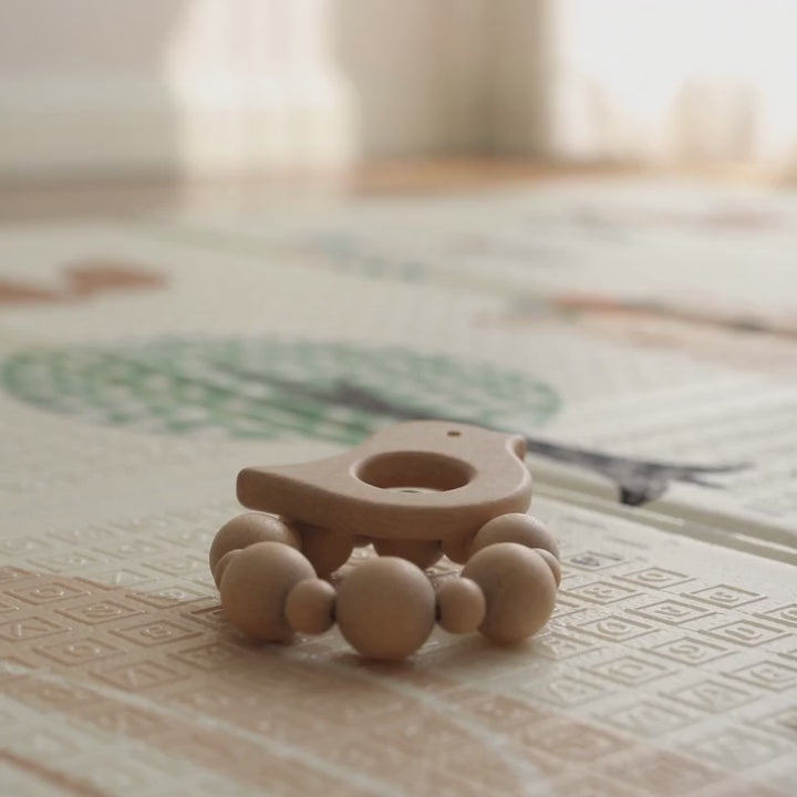 Main de bébé qui attrape l'anneau de dentition oiseau en bois sur un tapis de jeu ECLOA
